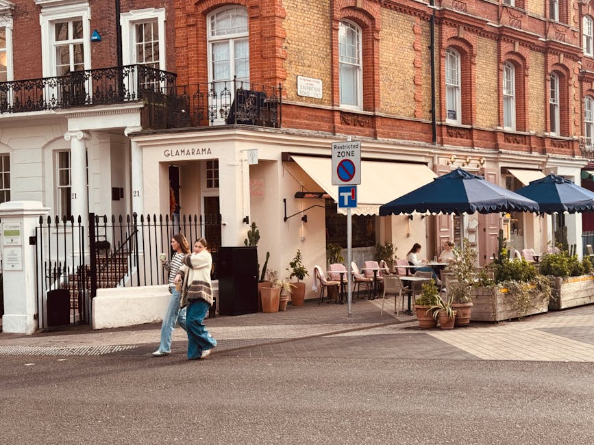 The image depicts a street view of a historic red brick building, part of a row of similar residential properties, with large windows featuring white trim and some with small balconies enclosed by bla
